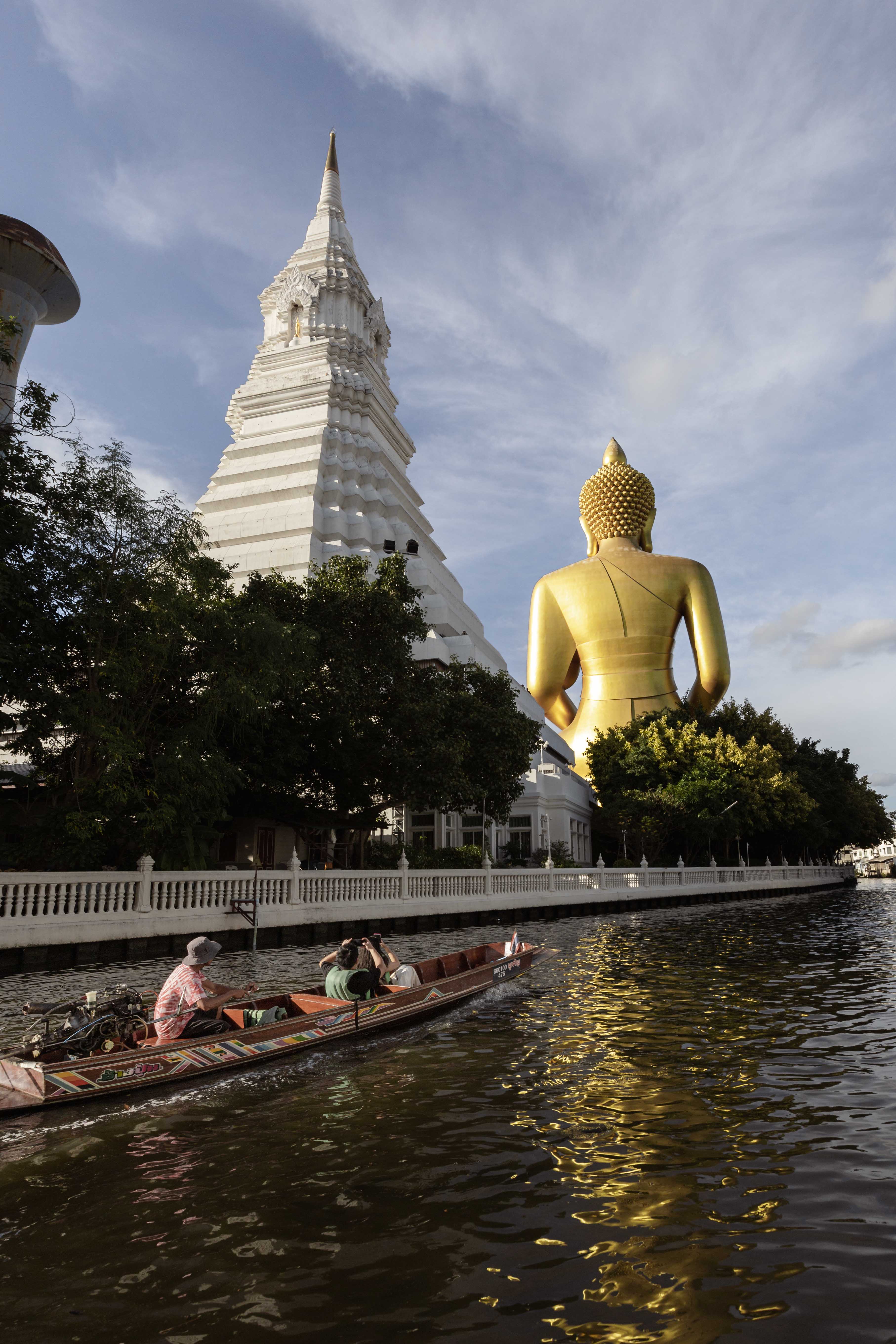 A longtail boat approaching the Giant Buddha and white chedi at Wat Paknam, Bangkok.