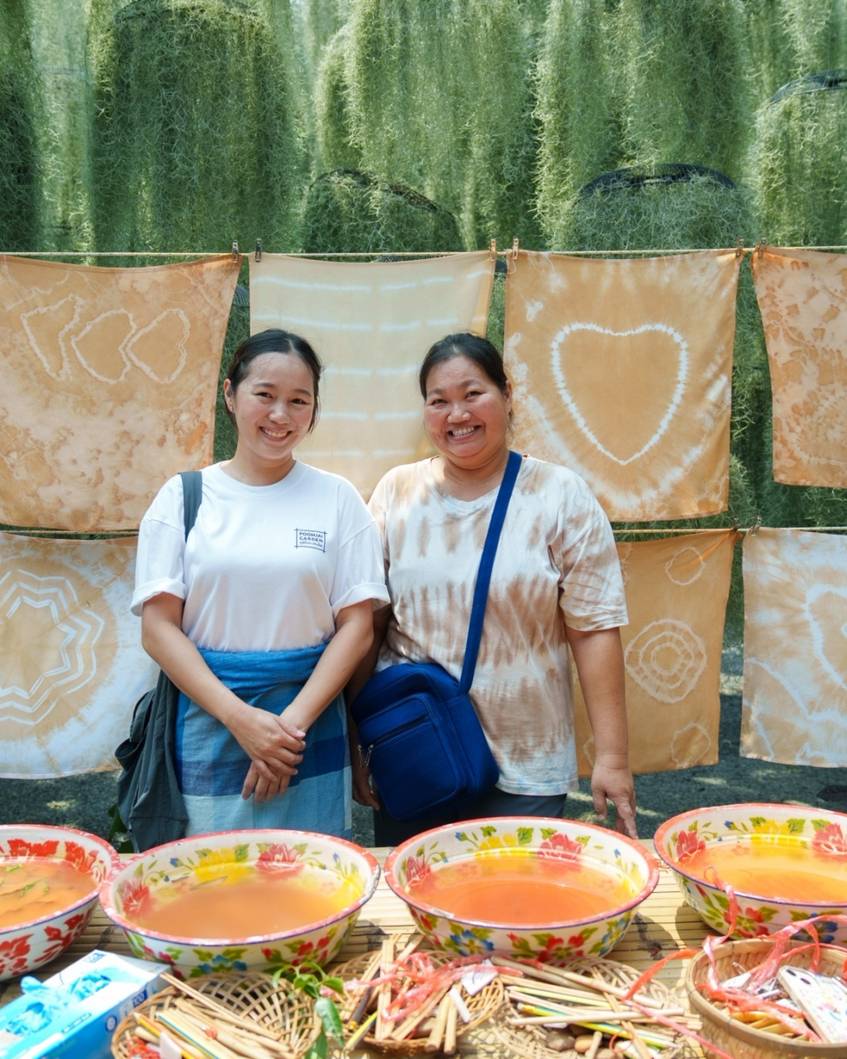 Two workshop hosts standing beside finished tie-dyed cloths and bowls of natural dye at Poomjai Garden.