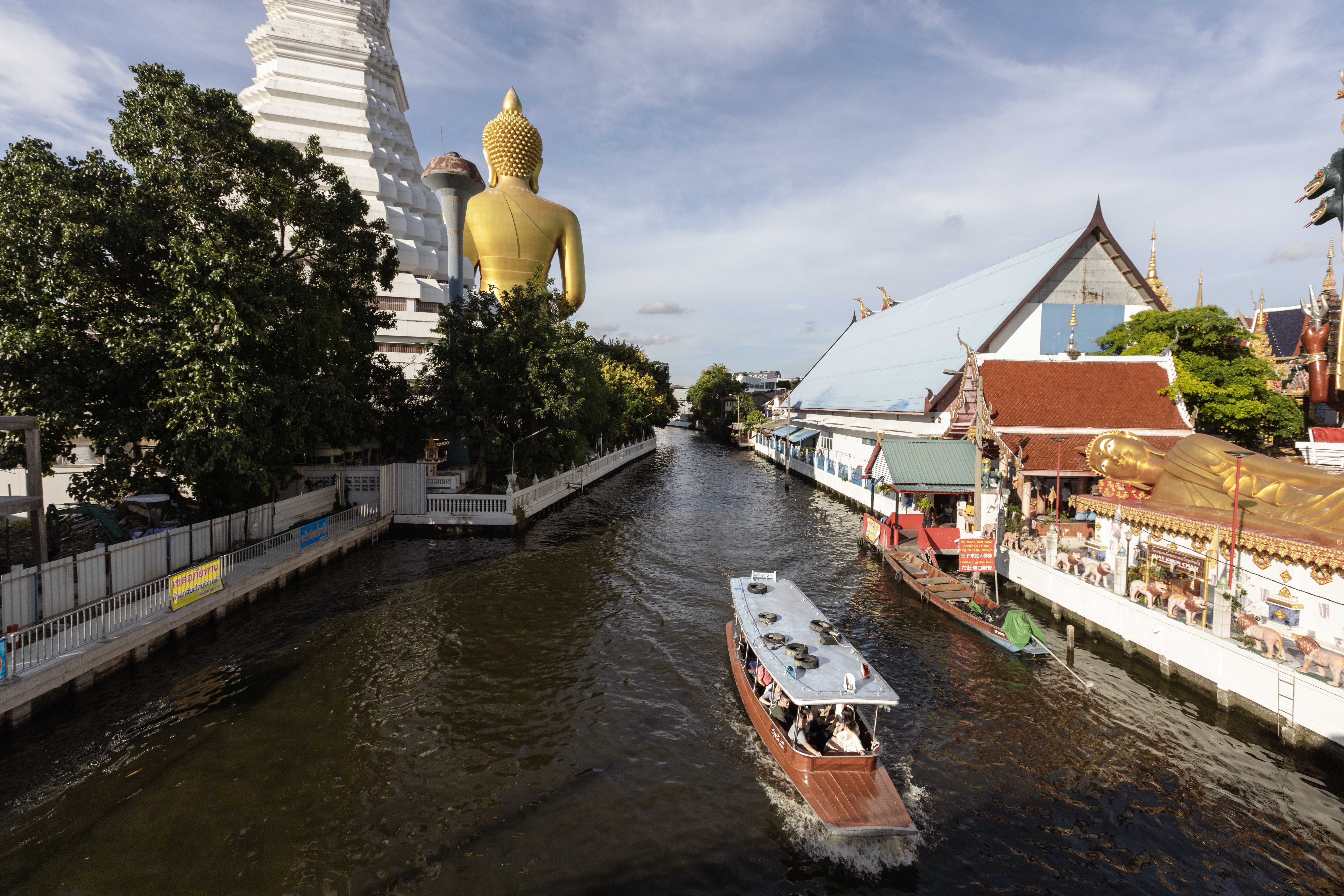 View from behind the Giant Buddha statue toward the canal, with a tour boat passing.