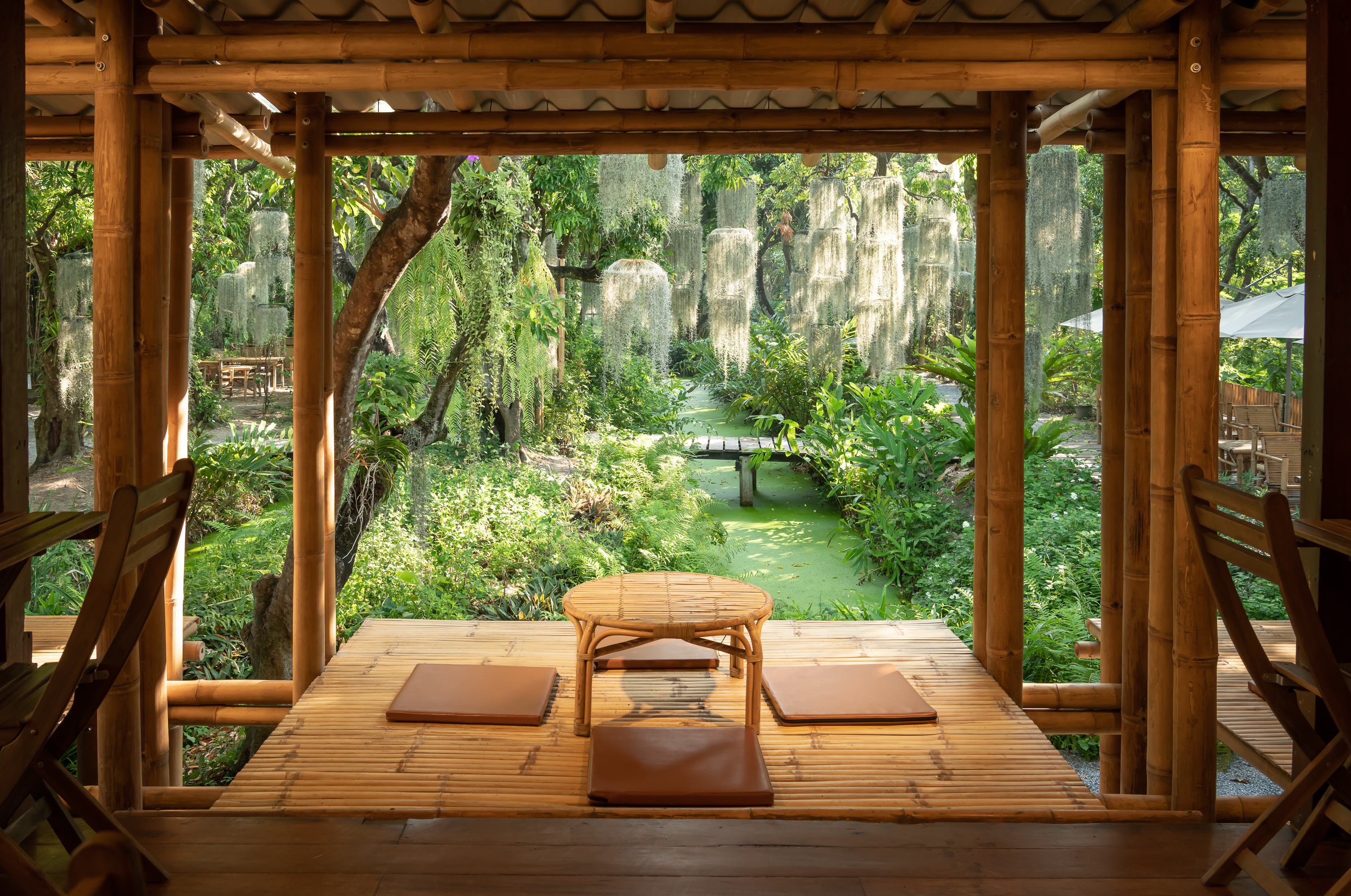 A raised bamboo pavilion seating area at Poomjai Garden overlooking a moss-draped canal garden.