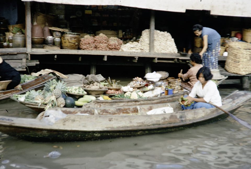 Archival photo of a floating market on the canal, vendors under blue umbrellas in boats.