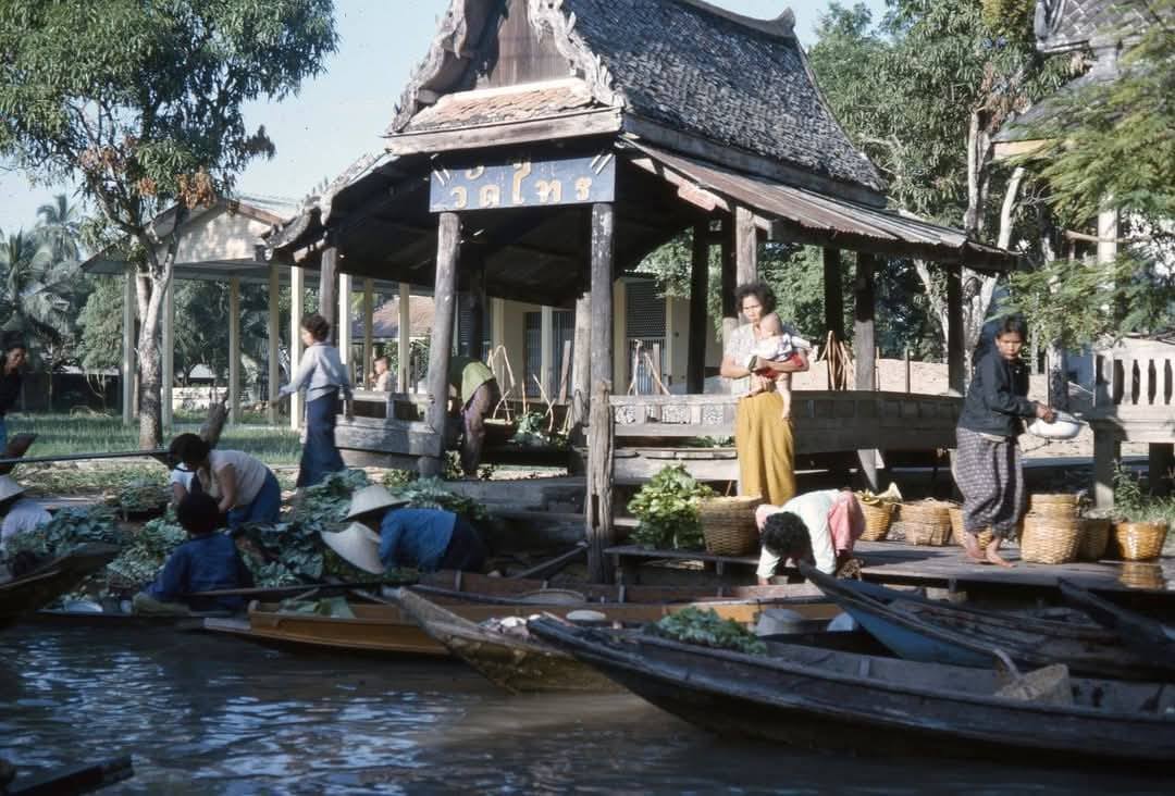 Archival photo of the Wat Sai pavilion on the canal, with boats loaded with produce and a mother holding a baby standing on the deck.