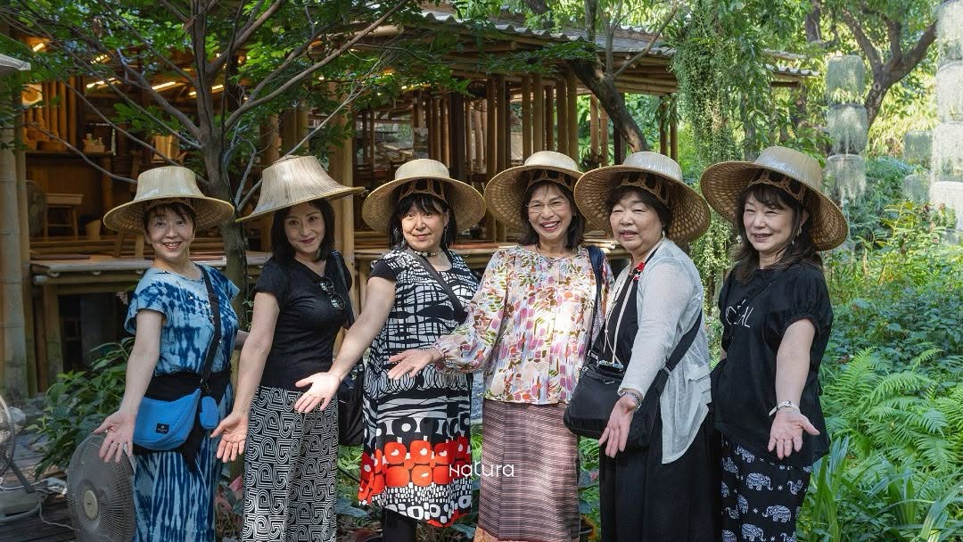 A group of guests wearing traditional hats posing together in the garden outside Natura Caf&eacute;.
