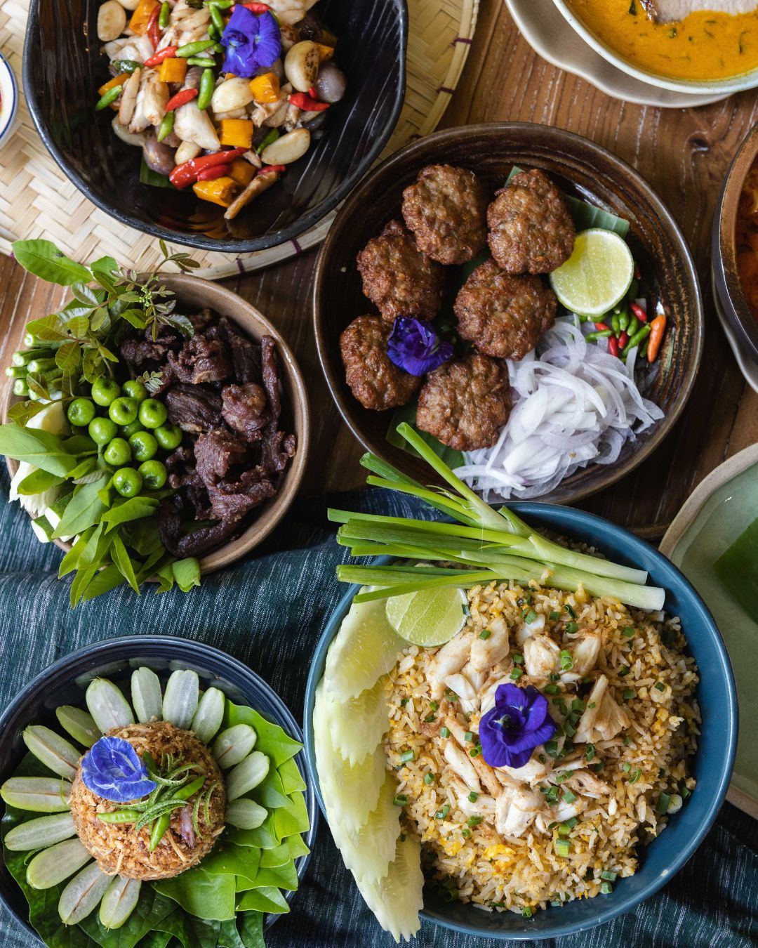 A spread of Thai dishes at Natura Caf&eacute; including crab fried rice, grilled pork, and stir-fried vegetables.